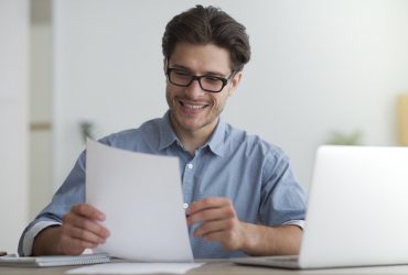 Happy Entrepreneur Reading Financial Report Sitting At Laptop